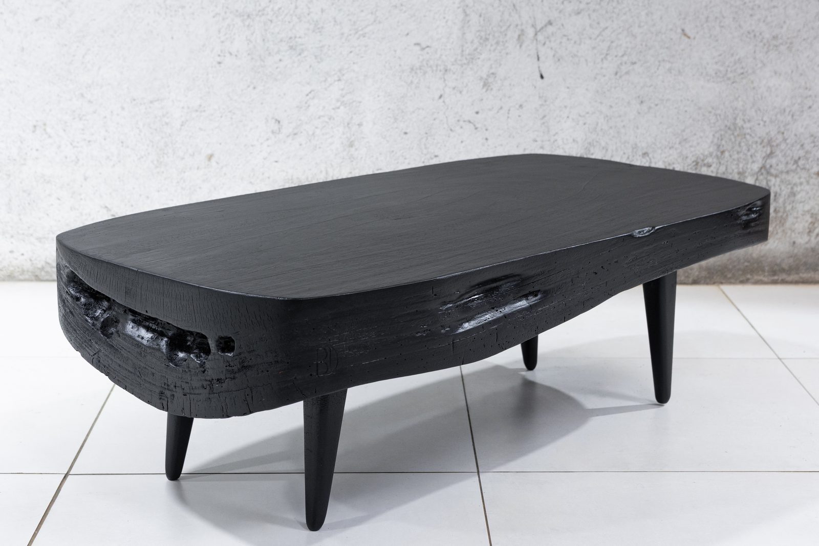 Sabana Brasa — Guanacaste coffee table finished by torch, matte black top with a charred live edge, on splayed turned legs