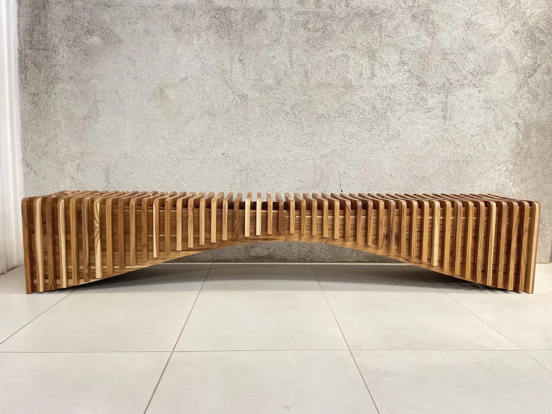 The Rib Bench seen at an angle, its stacked Guanacaste slats forming a low arch