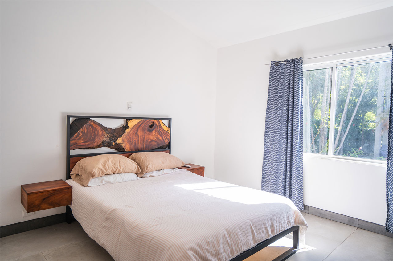Cama Refugio seen at an angle in a bright bedroom, floating Guanacaste nightstands on both sides