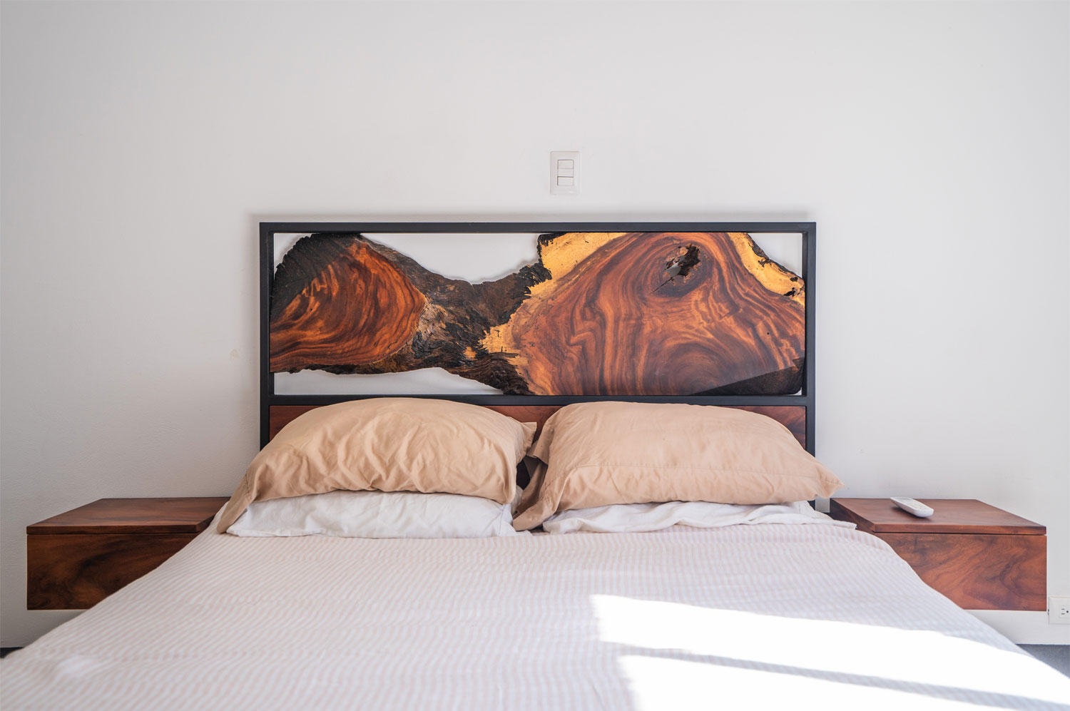 Close view of the Cama Refugio's live-edge Guanacaste headboard suspended in its blackened-steel frame