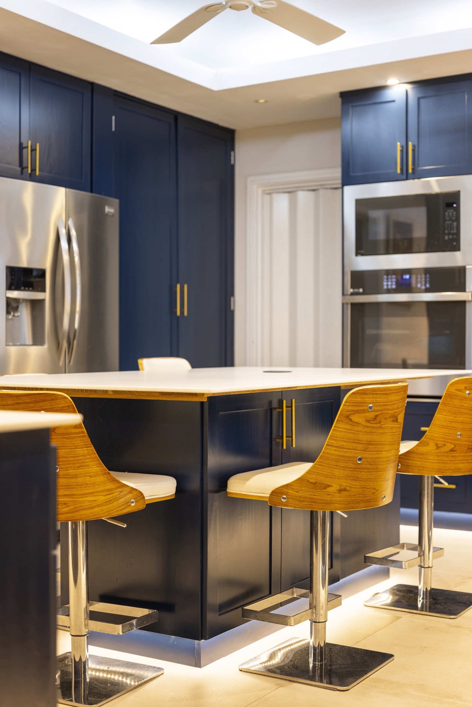 Jacamarca kitchen — navy cabinetry with a quartz waterfall island and wood bar stools