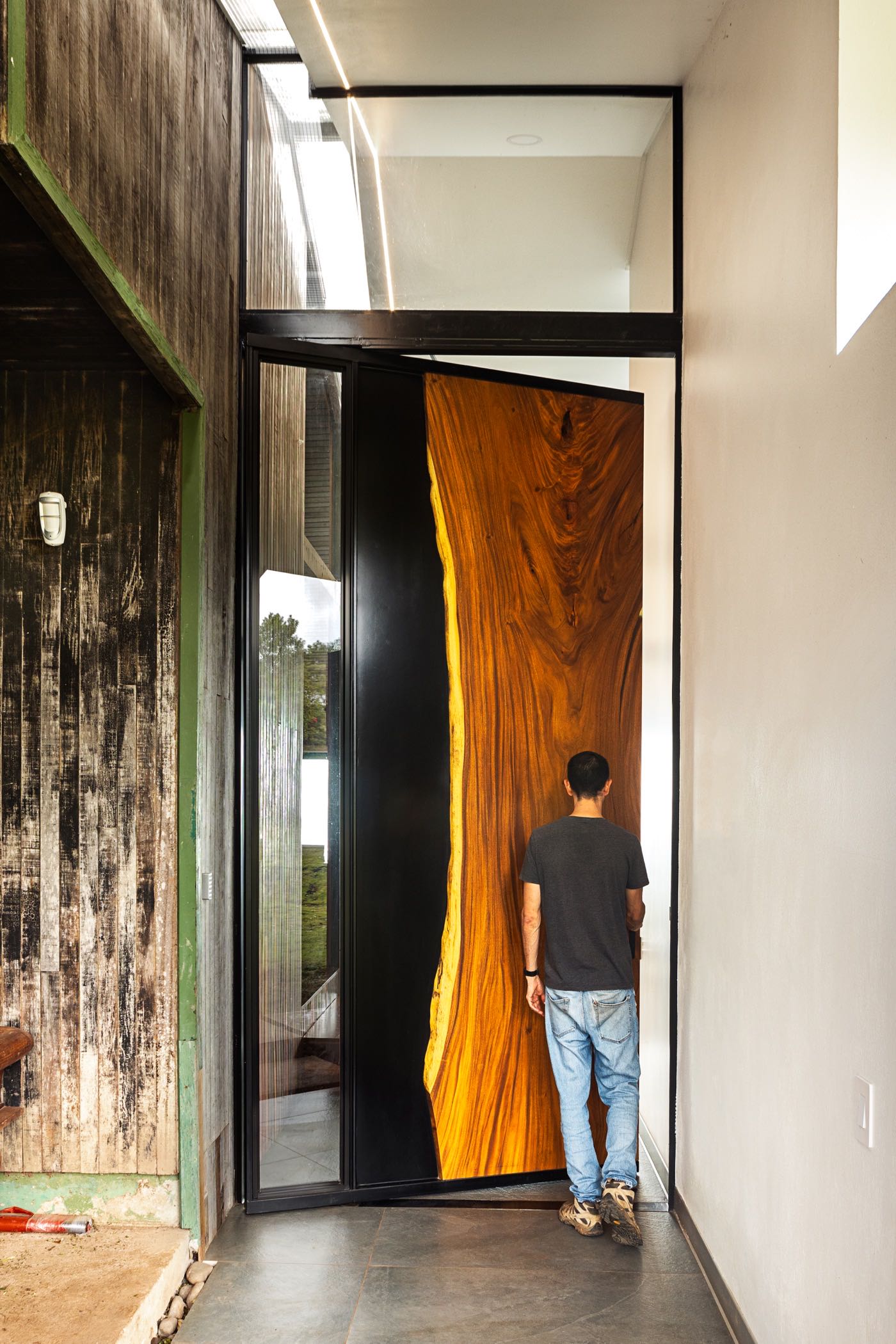 A person steps through the towering live-edge Guanacaste pivot door at Casa Santos, showing its full scale