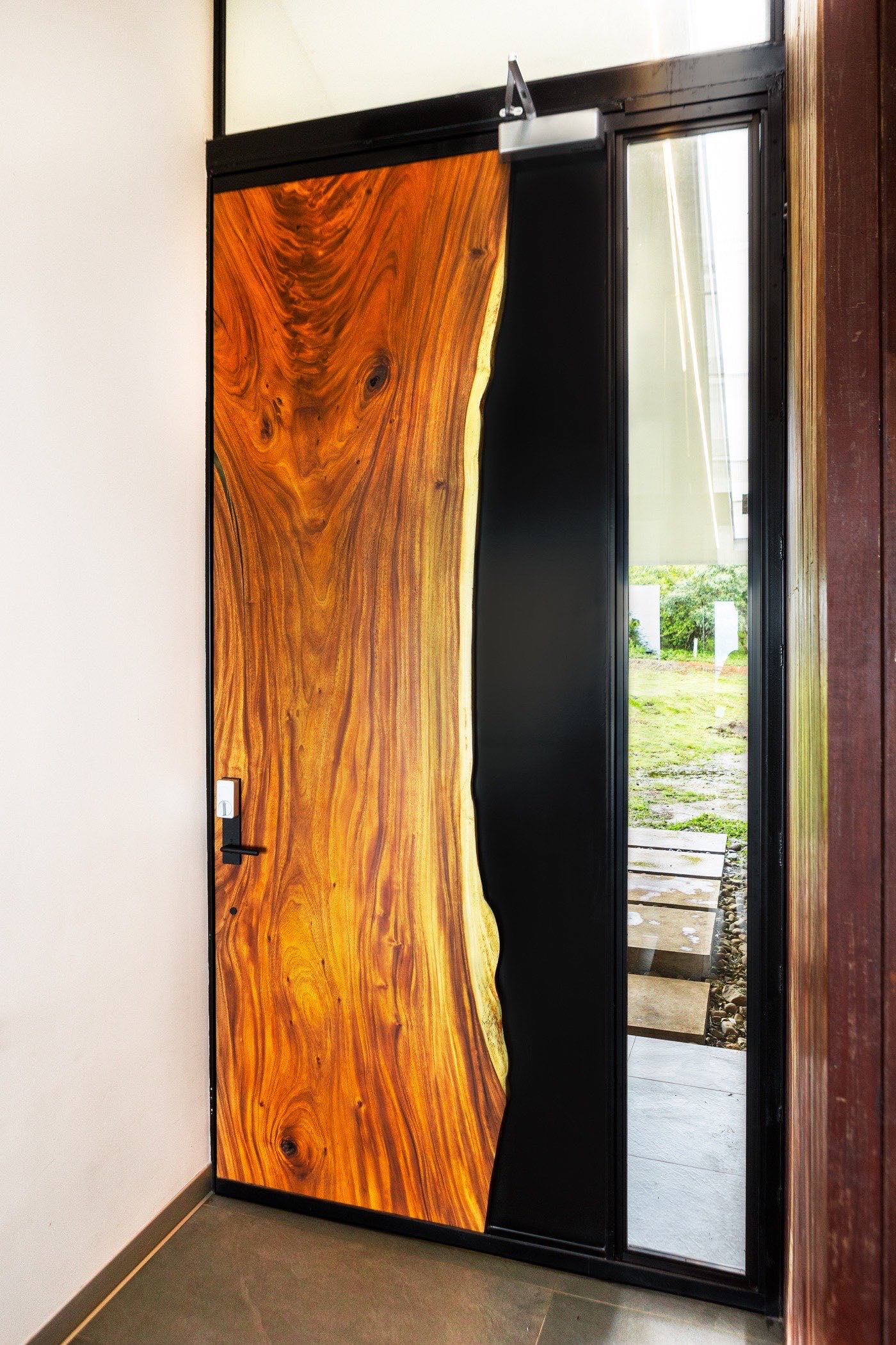 Reventazón door seen from inside — the live edge glowing where the Guanacaste slab meets the steel and glass sidelight